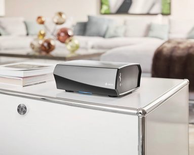 HEOS Amp HS2 sort hi-fi stereforstærker, set ovenfra, på hvidt sofabord foran lys grå sofa i moderne stue