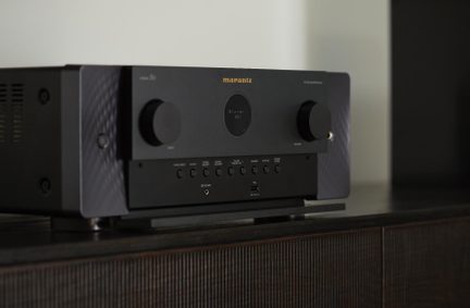 Zwarte AV-versterker van Marantz in metaal, driekwartzicht, twee grote knoppen, rond centraal display, USB-poort en hoofdtelefoonaansluiting