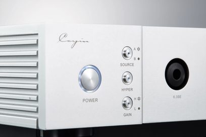 Vista ravvicinata del pannello frontale in alluminio argento del preamplificatore per cuffie Cayin IHA-8, con alette di ventilazione laterali, pulsante circolare di accensione con alone blu, tre mini-selettori metallici Source, Hyper e Gain e presa jack 6,3 mm 6.3SE