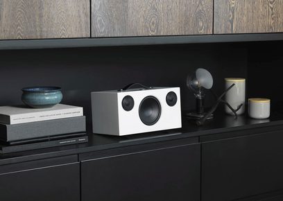 Enceinte sans fil Audio Pro ADDON C10 blanc, vue de face, posée sur un meuble noir avec livres et objets décoratifs