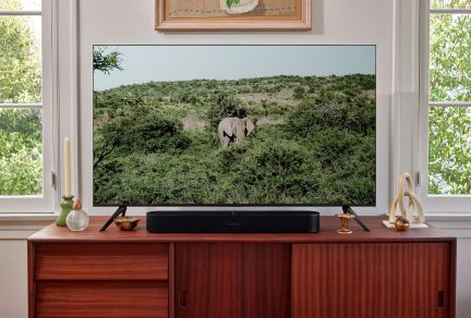 Televisor de pantalla plana sobre mueble de madera con barra de sonido negra, velas, jarrones, escultura y cuadro