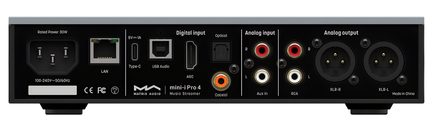 Kompakts matēti melns metāla audio korpuss, aizmugures skats, ar IEC strāvas savienotāju, Ethernet portu, USB‑C, USB‑B, HDMI ARC, optisko ieeju, oranžu koaksiālo ieeju, sarkanām/baltām RCA ieejām un RCA izejām, kā arī divām līdzsvarotām XLR izejām