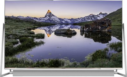 Bjergtsø der spejler en sneklædt top, omgivet af vegetation og klipper, ved solnedgang