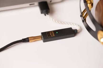 Lille, rektangulær audio-konverter i sort metal set fra oven, med et gyldent Hi-Res Audio-mærkat, udstyret med en grøn LED-indikator og forbundet med to sort-hvide snoede kabler