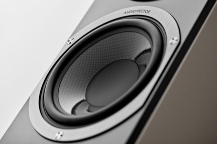 Nærbillede i trekvart vinkel af en grå hi-fi-højttaler med sort kegle i flettet tekstur og ramme i børstet aluminium fastgjort med fire skruer