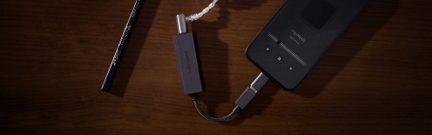 Cavo USB-C, adattatore da USB-C a jack audio da 3,5 mm e base di ricarica wireless, su una superficie in legno