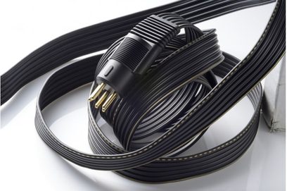 Sorte elektriske kabler oprullet i spiral, med forgyldte stik i enderne, på en hvid reflekterende overflade