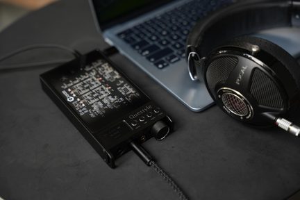 Fekete Questyle fejhallgató-erősítős DAC csatlakoztatva Focal Hi-Fi fejhallgatóhoz és szürke laptophoz sötét íróasztalon