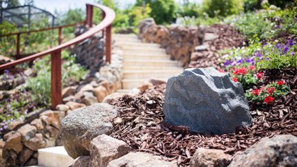 Diffusore da giardino camouflage a forma di roccia grigia in un'aiuola pacciamata ai bordi di una scala paesaggistica
