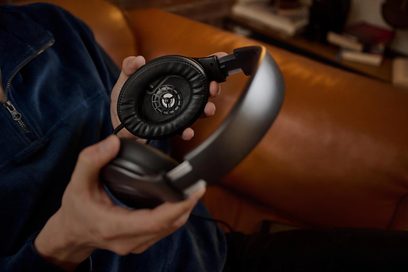 Sluten hi-fi-hörlurar Sennheiser HD 620S hållna av två händer, högra öronmusslan öppen, grovbild, lätt sidovinkel
