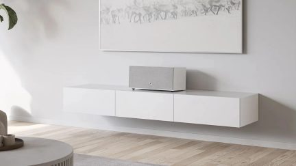 Fehér, falra szerelhető TV-szekrény három fogantyú nélküli rekesszel, tetején egy szürke hangszóróval
