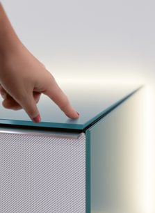 Palec naciskający na metaliczną, szarą, perforowaną przednią część szafki audio-wideo z metalicznym wykończeniem