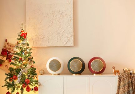 Un albero decorato a sinistra, tre altoparlanti sferici bianchi, verdi e rossi su un mobile bianco, quadro con texture sulla parete