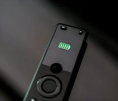 Batería externa negra con pantalla que muestra un icono de carga verde y botón circular en primer plano