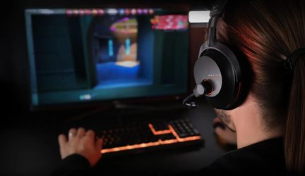 Cască de gaming Beyerdynamic MMX 150 neagră cu microfon, jucător de PC văzut din spate în fața ecranului și a tastaturii iluminate din spate