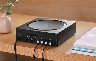 Čierny stereo hi-fi zosilňovač Sonos Amp, pohľad spredu, konektory na zadnej strane, otočný gombík na vrchu, položený na drevenom stole