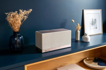 Beige rectangular Triangle smart speaker with perforated front, front view on a blue cabinet