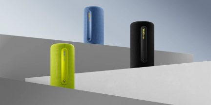 Prenosni cilindrični Bluetooth zvočniki v modri, črni in zeleni barvi, pogled od spredaj na sivih geometrijskih stojalih