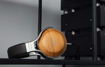 Denon AH-D9200 hovedtelefoner i lyst træ, set fra venstre profil liggende på en sort holder, med lukkede ørepuder i sort læder