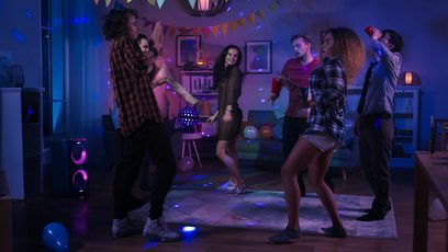Gruppe unge voksne, der danser i en stue dekoreret med balloner og farverige lys, festlig stemning
