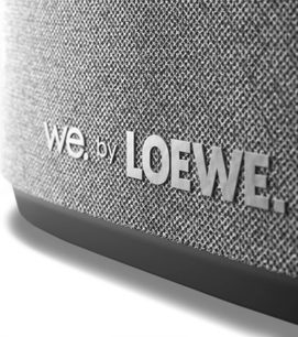 Prim-plan al grilei gri a unei boxe compacte Loewe We. BOOST, cu logo-ul We. by LOEWE în relief