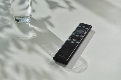 Czarny pilot Samsung leżący na błyszczącej powierzchni obok szklanki wody, widok z góry