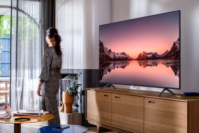 Samsung QE75Q60T 2020 televisie met een berglandschap bij zonsondergang op het scherm, geplaatst op een licht houten meubel