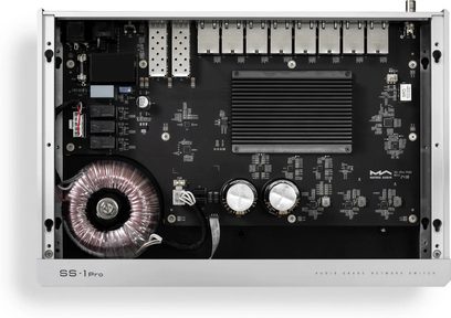 Switch de red Matrix Audio SS‑1 Pro gris plateado de aluminio, vista superior con la tapa retirada, placa base negra con ocho módulos SFP metálicos alineados, disipador de calor negro con aletas, transformador toroidal desnudo y dos condensadores cilíndricos plateados