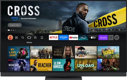 Vista frontal del televisor de alta definición Panasonic TV-77Z95B, marco negro de metal cepillado con bordes finos, colocado sobre una base central discreta, pantalla ancha que muestra una interfaz de streaming con iconos coloridos