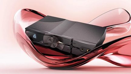 Černý sluchátkový DAC zesilovač iFi Audio s velkým čelním ovladačem hlasitosti, na futuristickém pozadí z růžového skla