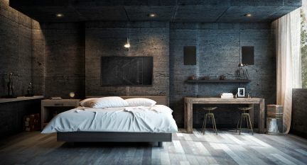 Modernt sovrum i industriell stil, betongväggar, låg grå säng, skrivbord och pallar i trä, dämpad belysning