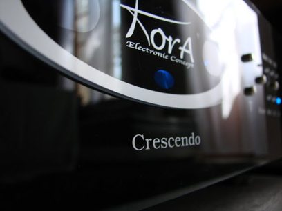 Kora Crescendo stereoforstærker, nærbillede af forsiden i børstet aluminium med logo og oplyst blå knap
