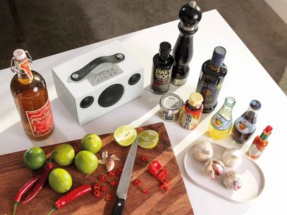 Trådløs høyttaler Audio Pro ADDON C3 hvit, lime, røde chilier, hvitløk, kniver, alkoholflasker og krydder på trekuttebrett