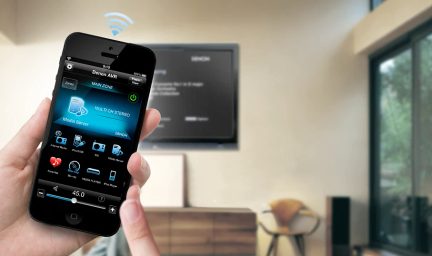 Mano che tiene uno smartphone che mostra l'app Denon AVR per controllare un amplificatore home theater, primo piano