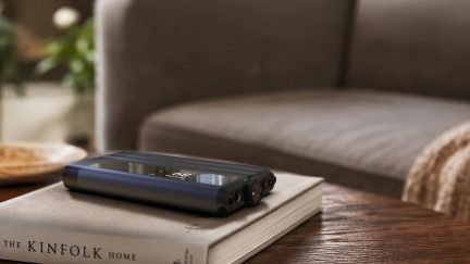 Lettore audio digitale nero con schermo e doppie uscite per cuffie, appoggiato su un libro da tavolino