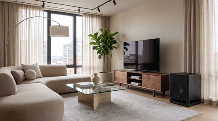 Černý subwoofer umístěný na podlaze vedle dřevěného televizního stolku v moderním obývacím pokoji