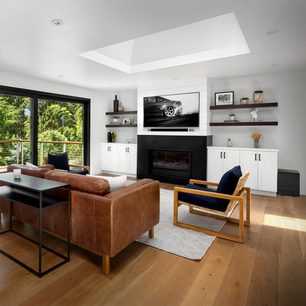 Moderne woonkamer met bruine lederen bank, blauwe fauteuil, open haard, donkere houten boekenkasten, grote glazen pui en lichte houten vloer