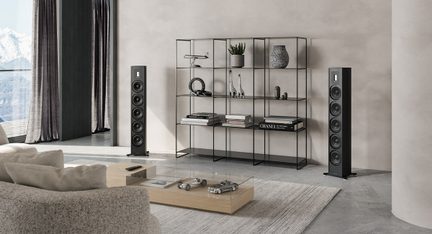 Moderne stue med beige sofa, træ sofabord, sort metalreol, 2 sorte højttalere, gråt tæppe