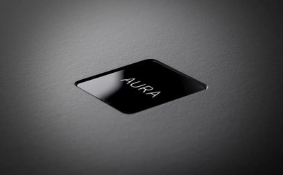 Rega Aura MC black phono preamp, top-down 45-degree angled view, glossy surface, white "Aura" inscription