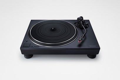 Aukštos kokybės „Technics SL-1500CEG-K" juodos spalvos vinilo plokštelių grotuvas, šiek tiek įžambiai nufotografuotas iš viršaus, su apvaliu besisukančiu padėklu ir nuskaitymo švytuokle