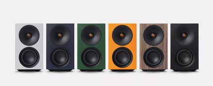 Compacte boekenplankspeakers in modern design op een rij, fronten in wit, blauw, groen, oranje, hout en zwart, met ronde zwarte luidsprekers
