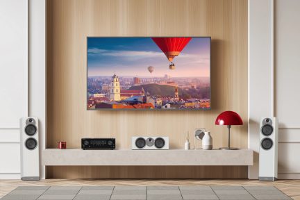 Fladskærms-tv, der viser et luftfoto af Vilnius med varmluftsballoner i en lyserød himmel, på et lavt, lyst træmøbel
