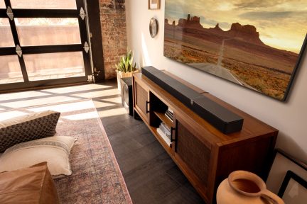 Schwarze Soundbar auf einem braunen TV-Möbel mit passendem Subwoofer daneben