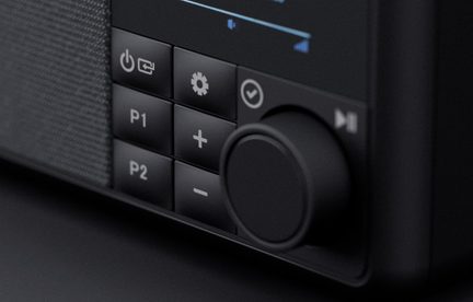 Matně černý ovládací panel, plast a tkanina, pohled ze tří čtvrtin, velký otočný knoflík, tlačítka P1, P2, +, -, zapnuto