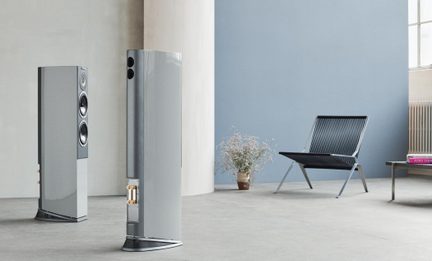 Par af lysegrå gulvhøjttalere med lakeret finish, set i trekvart vinkel forfra og bagfra, slanke kabinetter på skrå base med frontpanel udstyret med bånddiskant og to woofere med metalringe, bagside med to runde basreflekshuller og forgyldte terminaler
