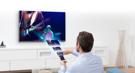 Muž zozadu ukazujúci diaľkovým ovládačom na televízor zobrazujúci gitaristu na pódiu