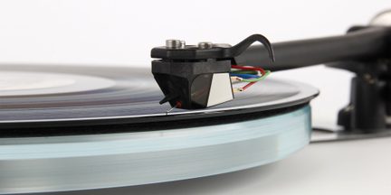 Vista laterale di un giradischi con braccio nero, testina nera, fili colorati, disco in vinile nero ed etichetta bianca