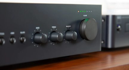 Czarny wzmacniacz hi-fi widziany z bliska, z dużym pokrętłem głośności, regulacją tonów niskich, wysokich i balansu oraz kontrolkami świetlnymi