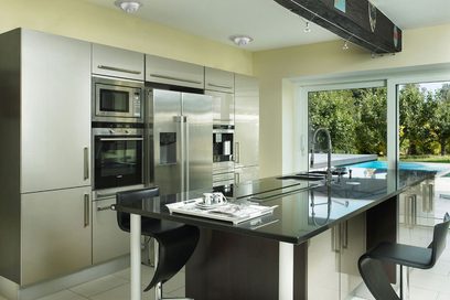 Cuisine moderne avec îlot central noir, électroménagers en acier inoxydable, grandes fenêtres et piscine extérieure visible