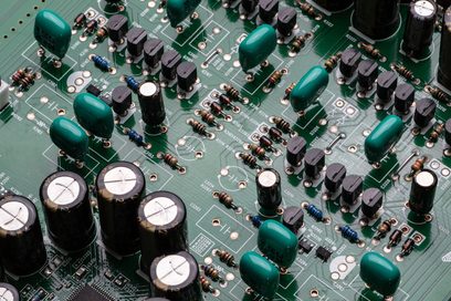Placa de circuito impresso verde com numerosos componentes eletrônicos redondos prateados e verdes, vista aproximada de cima